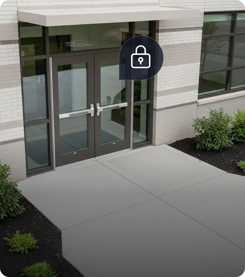 Double glass doors with push bars on a modern building entrance, surrounded by beige brick walls and small green bushes.