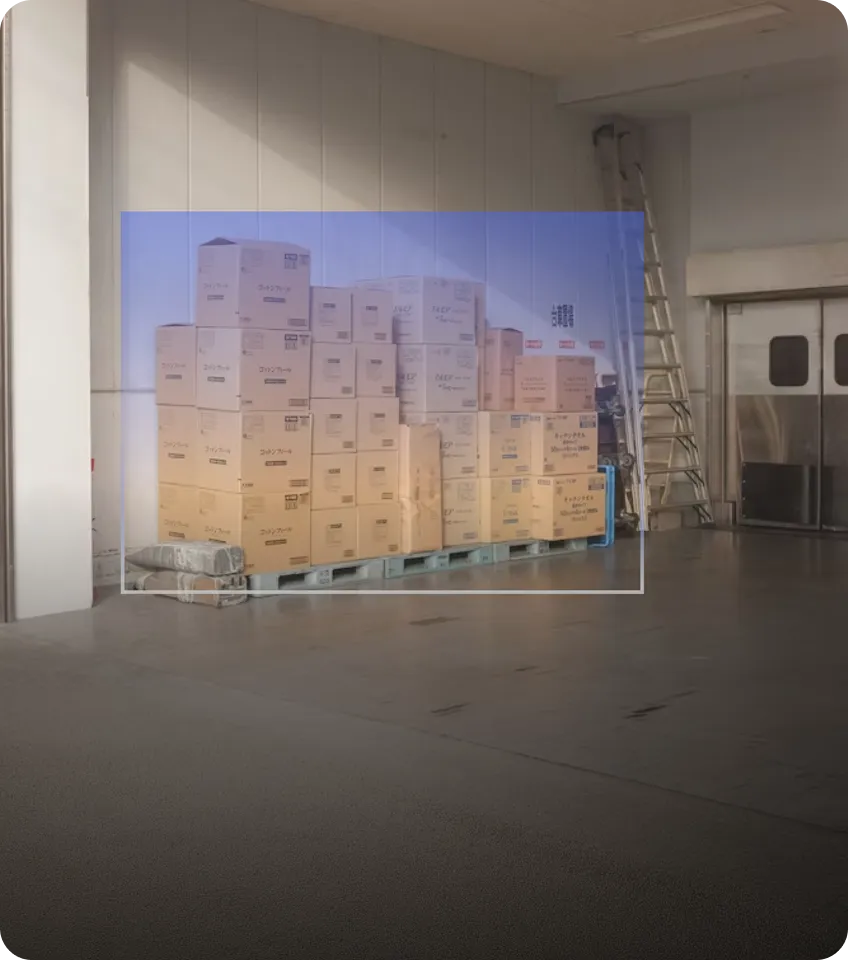 Stacked cardboard boxes on a blue pallet inside a warehouse area with a metal ladder and closed metallic doors in the background.