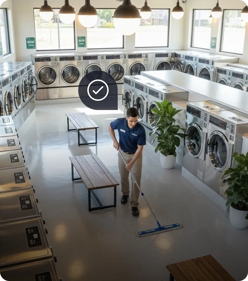 Man mopping the floor inside a bright laundromat with rows of washing machines and benches.