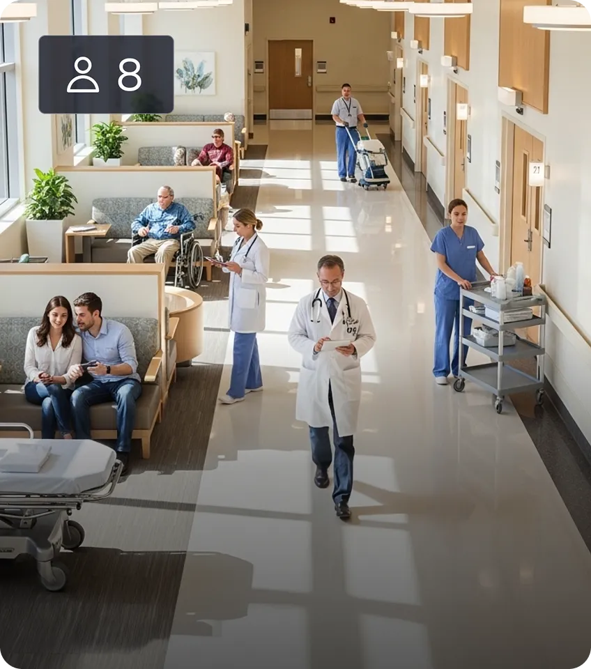 Hospital hallway with doctors, nurses, and patients seated in waiting area, including a man in a wheelchair and a couple sitting together.