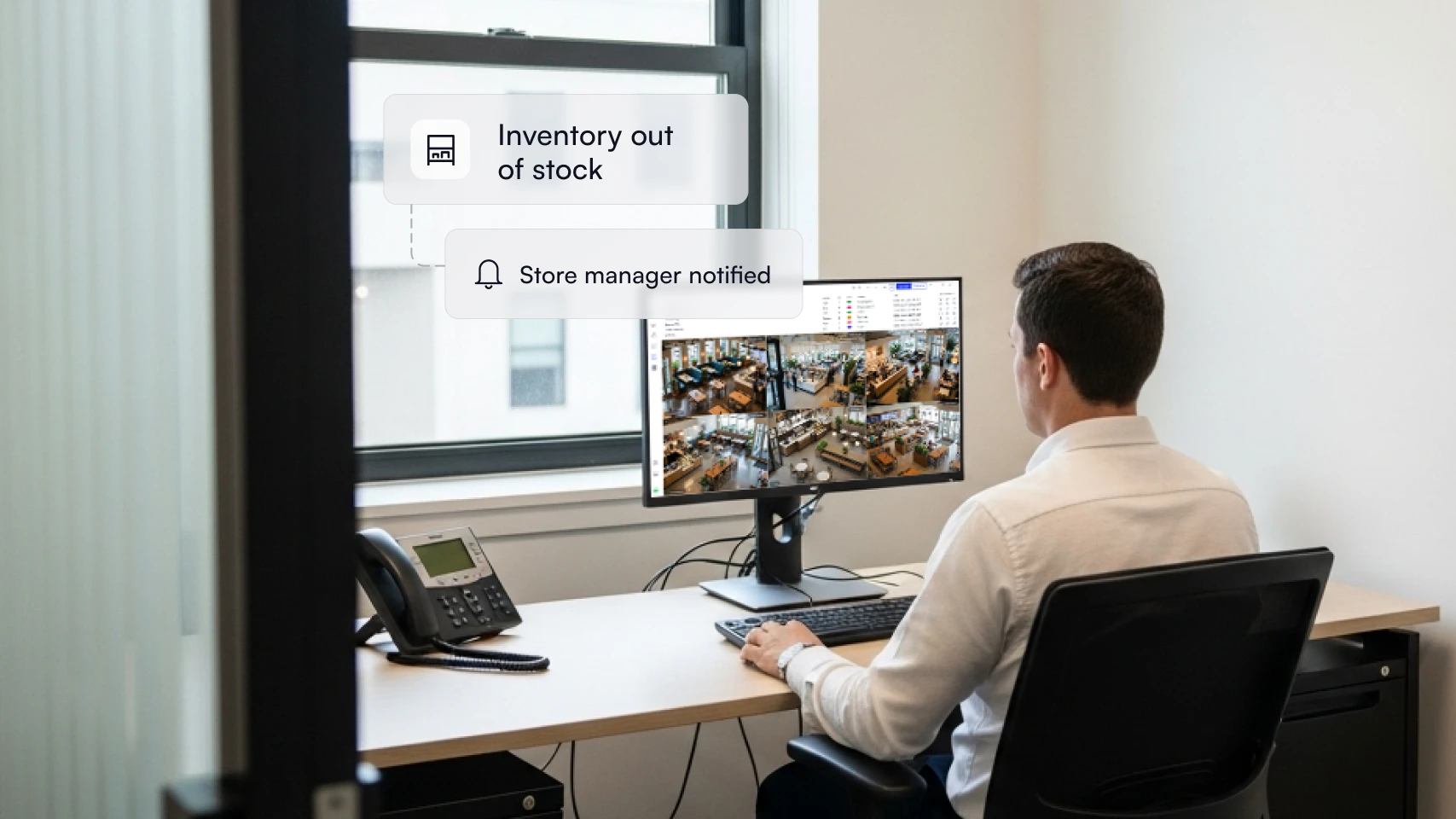 Man in a white shirt sitting at a desk in an office, monitoring multiple security camera feeds on a computer screen, with overlay notifications reading 'Inventory out of stock' and 'Store manager notified'.