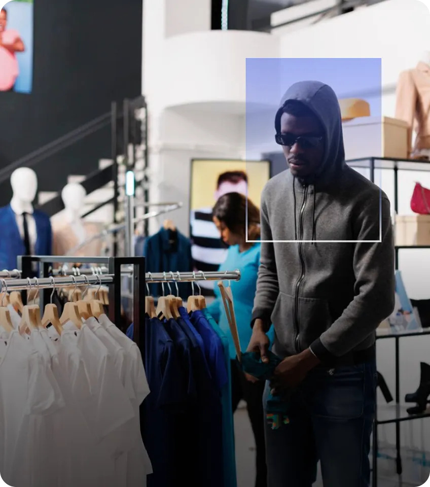 Man in a gray hoodie and sunglasses browsing clothes in a modern retail store.