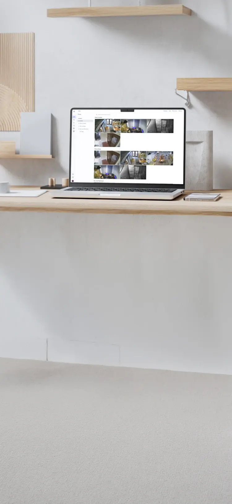 Laptop on wooden desk displaying multiple security camera surveillance feeds in a minimalistic room.