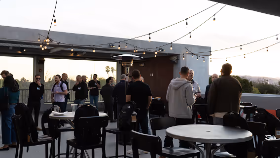 People socializing outdoors on a rooftop patio decorated with string lights during early evening.