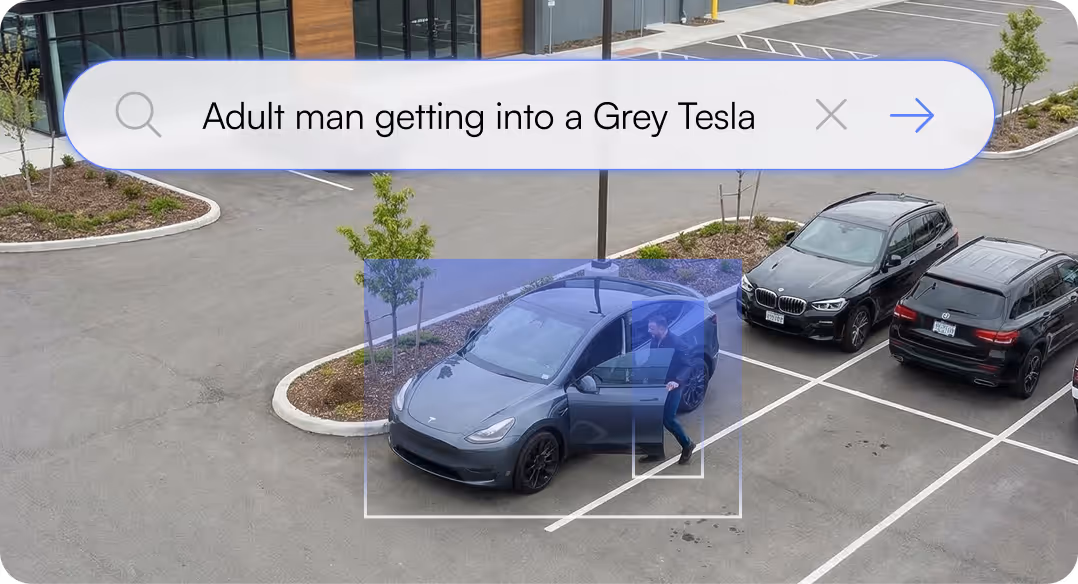 Adult man opening door and getting into a grey Tesla parked in an outdoor parking lot surrounded by other vehicles.