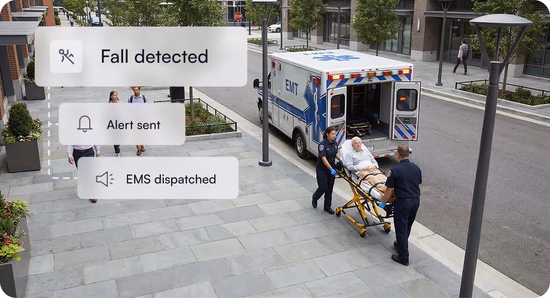 Emergency medical technicians pushing an elderly man on a stretcher toward an ambulance on a city sidewalk, overlaid with notifications indicating fall detected, alert sent, and EMS dispatched.