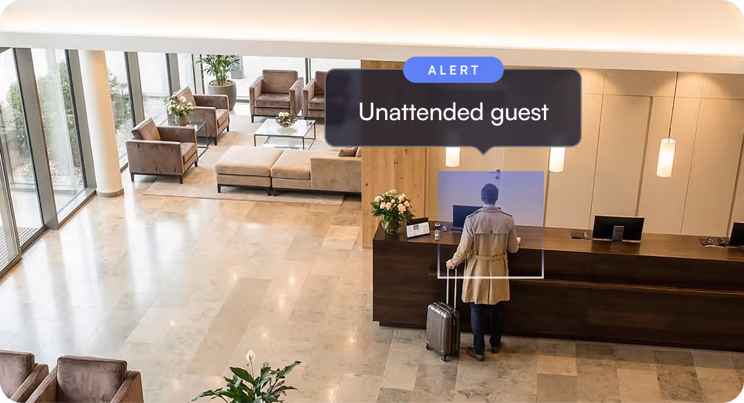 Hotel lobby with a person in a beige coat and suitcase standing at the reception desk, highlighted by a digital alert stating 'Unattended guest'.