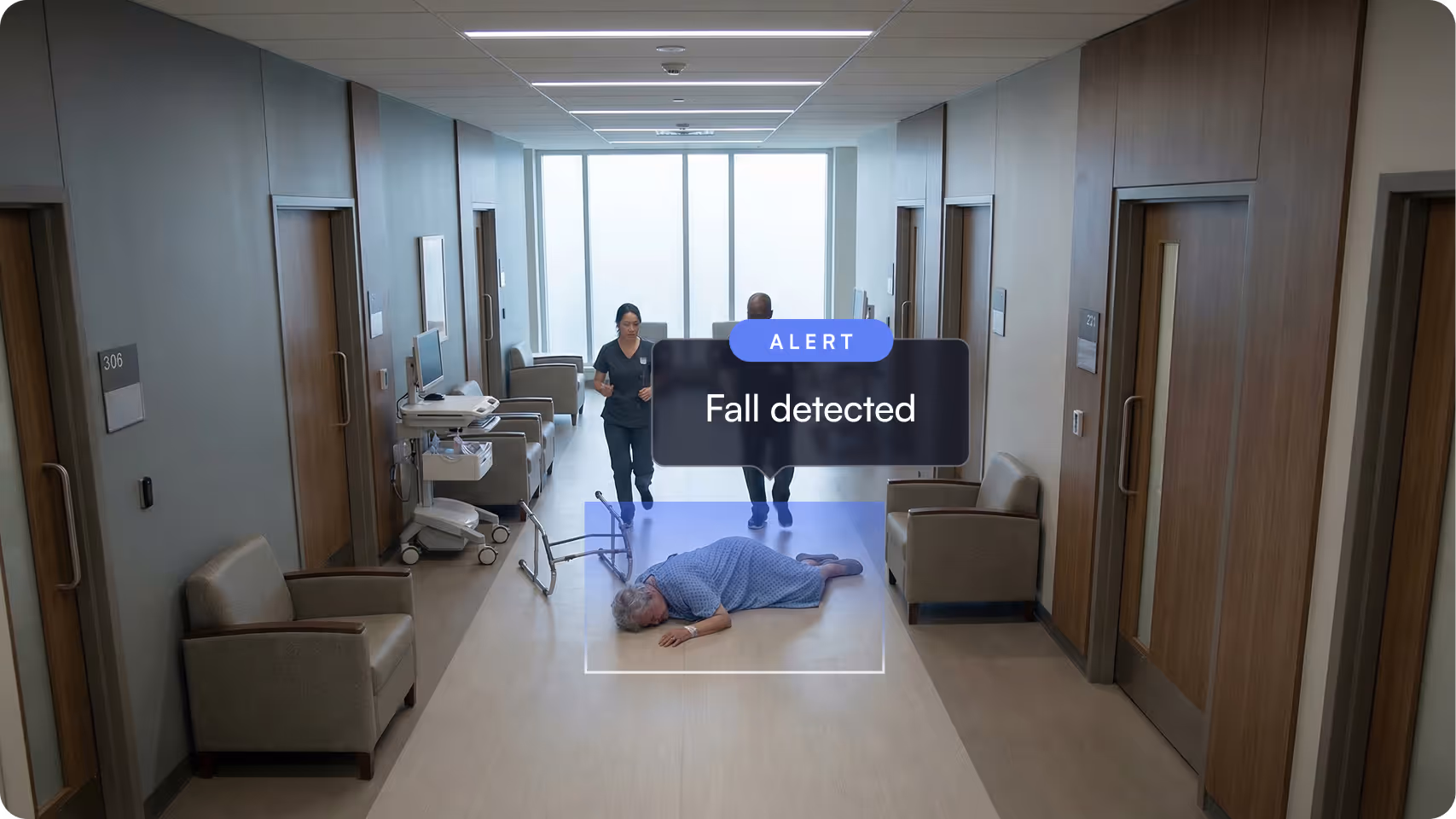 Elderly woman lying on the floor of a hospital corridor with a fallen walker, two medical staff walking quickly towards her, with an alert message reading 'Fall detected.'