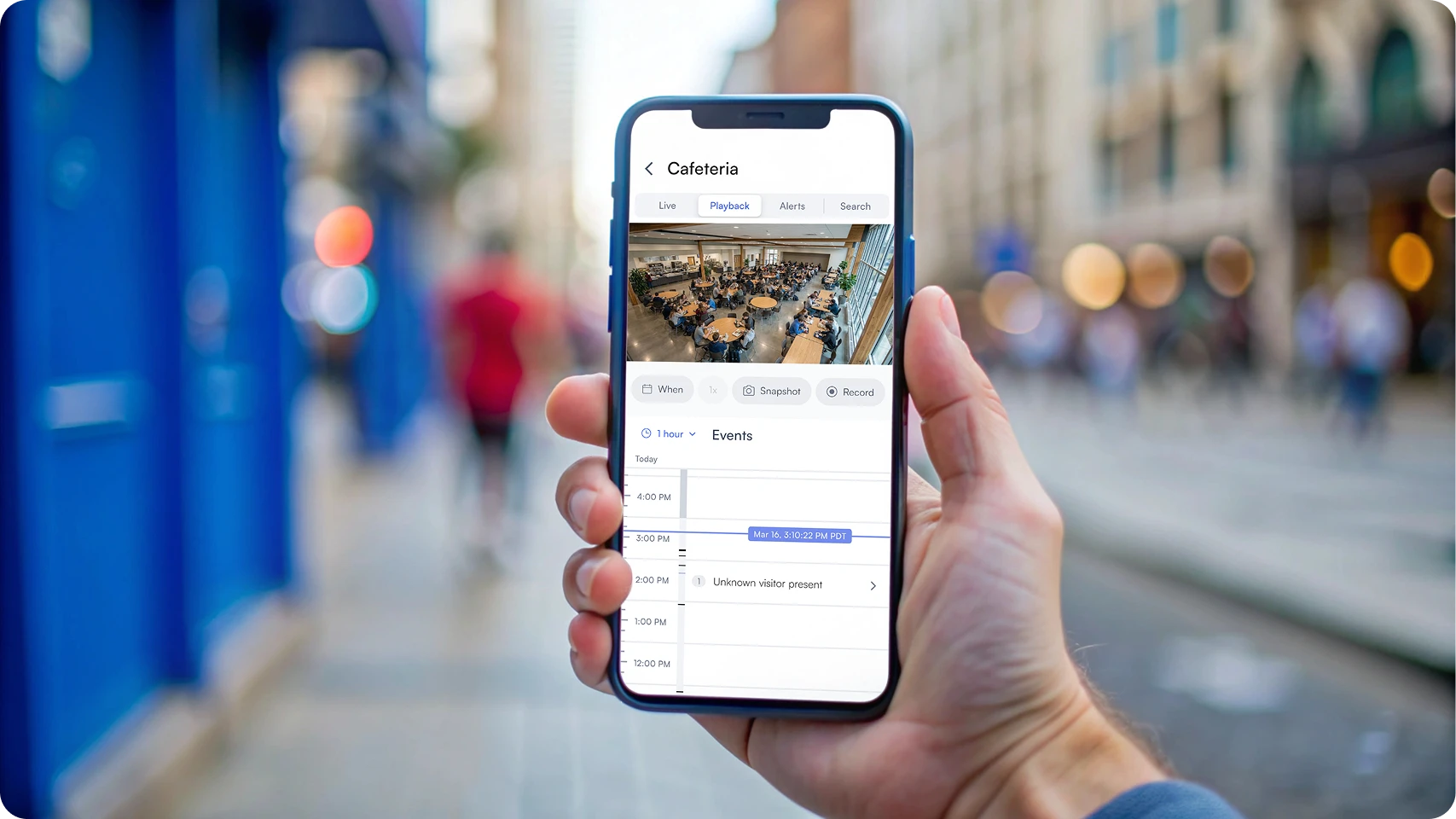 Smartphone screen showing a cafeteria surveillance camera playback with a timeline and an event labeled 'Unknown visitor present.'
