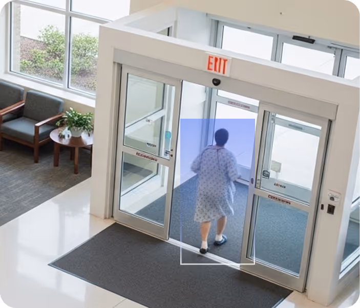 Person in a hospital gown walking through an automatic exit door at a medical facility entrance.