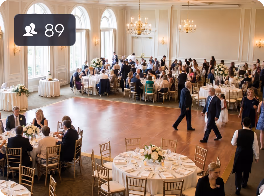 Event with people seated at round tables and a wooden dance floor in a large, elegant room.