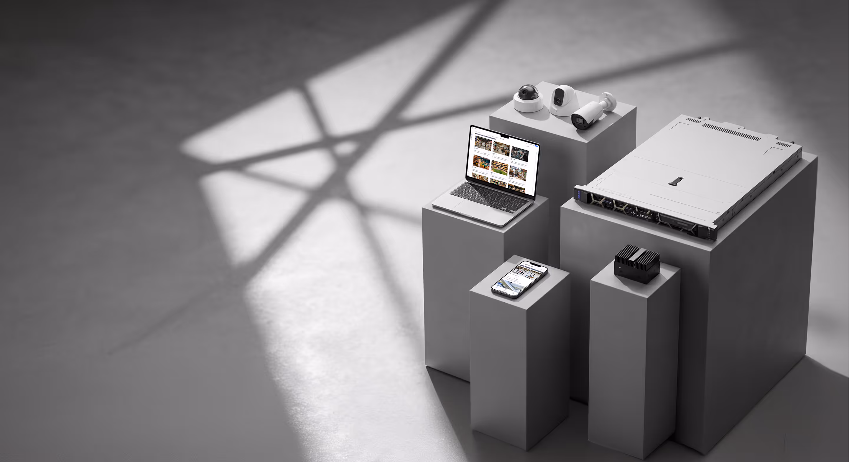 Security cameras, laptop, smartphone, and server on gray pedestals under geometric light shadows.