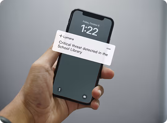 Hand holds phone showing alert: Critical threat detected in the School Library at 1:22 on October 6.