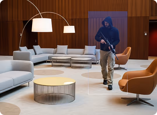 Man in hoodie holding rifle in modern living room with gray sofas and brown armchairs.