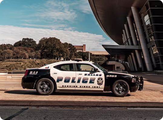 Side view of a black and white Dallas Police car parked outside a modern building.