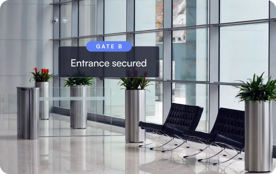 Modern secured entrance labeled Gate B with metal barriers, large windows, plants, and black chairs.