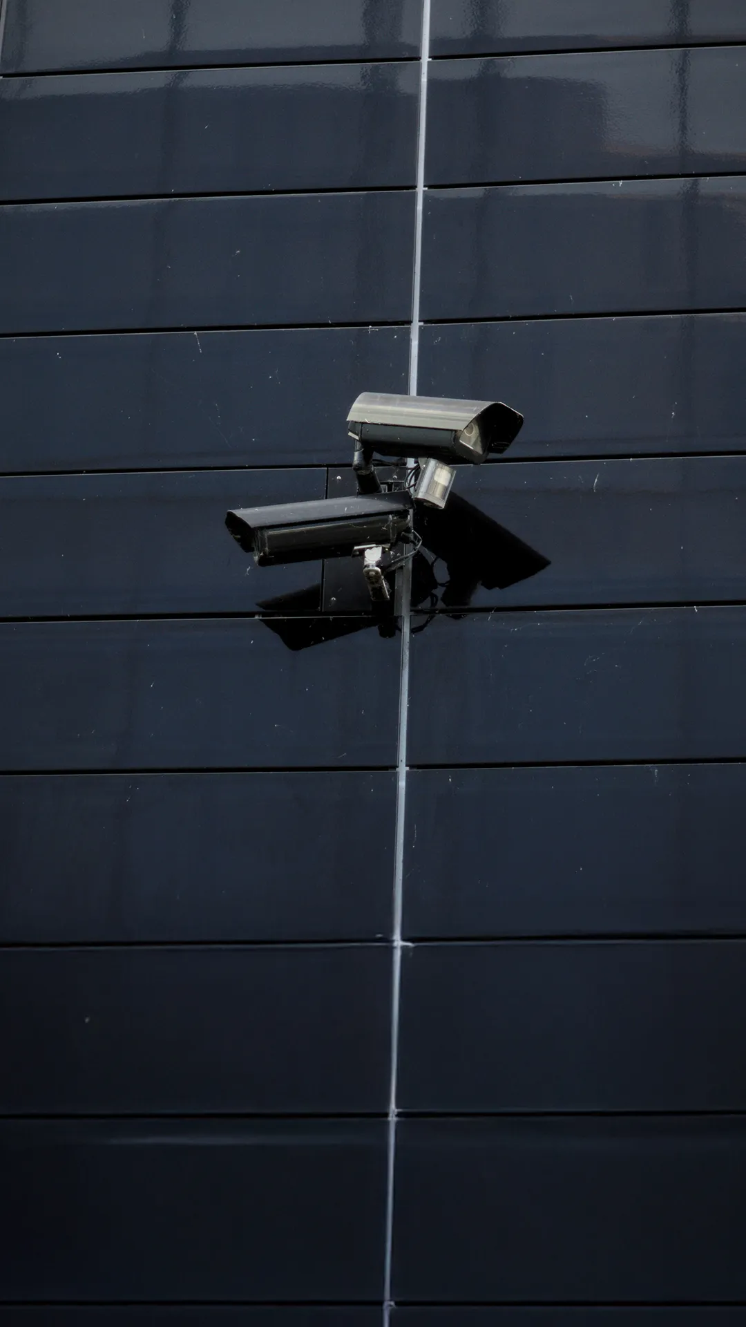 Two security cameras mounted on a dark tiled wall, angled differently for surveillance.