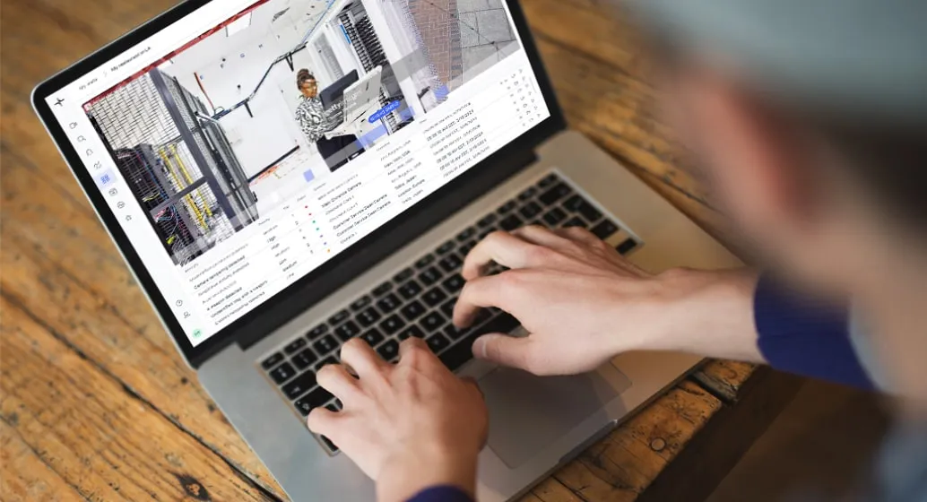 Person typing on a laptop showing security cameras and data on screen.
