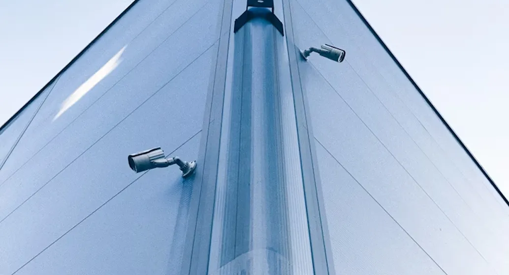 Two security cameras mounted on the corner of a modern building with glass and metal panels.