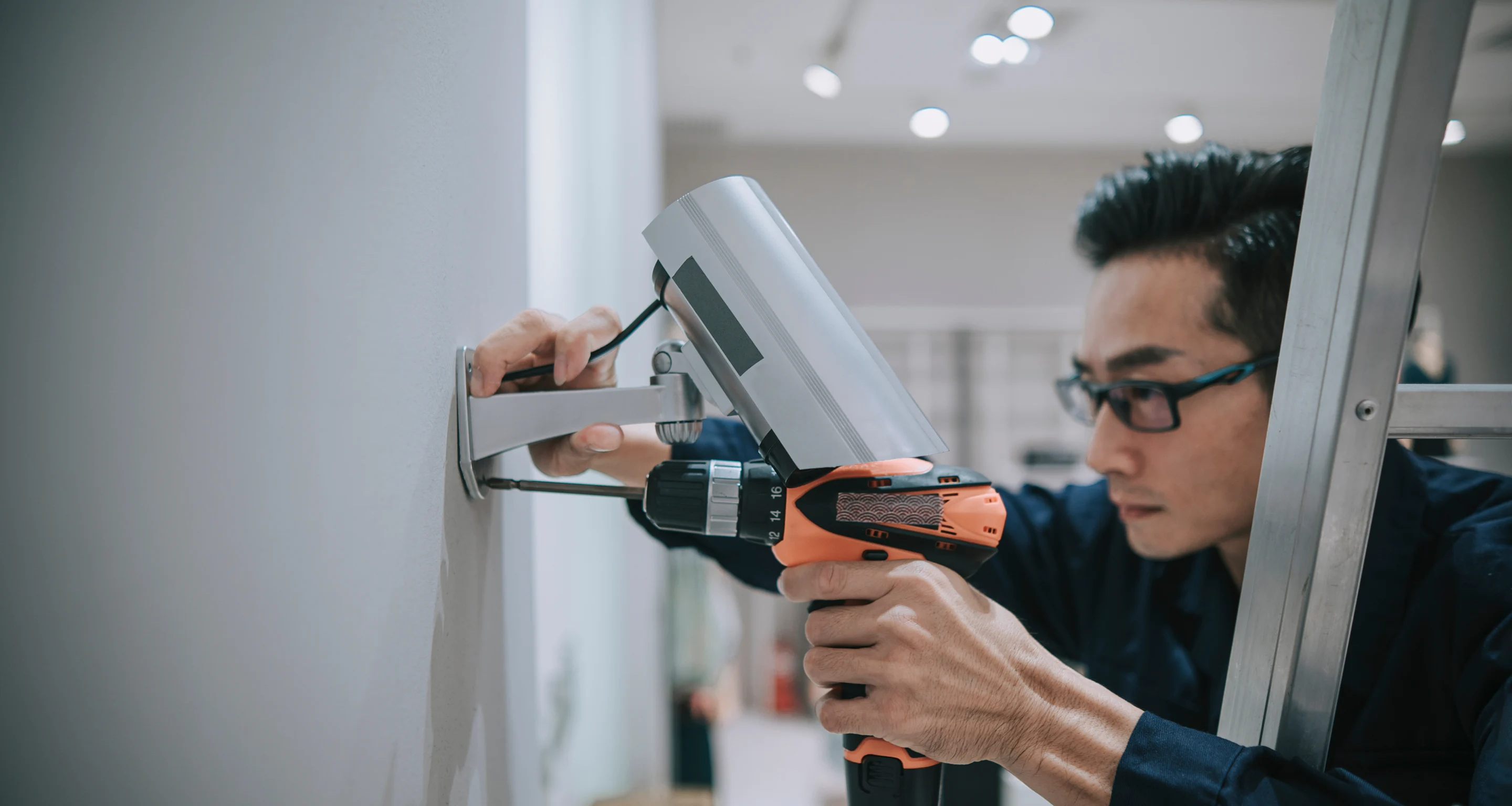 Technician using an electric drill to install a security camera on a wall.