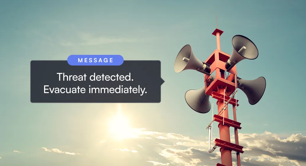 Red emergency alert loudspeakers mounted on a pole against a cloudy sky at sunset.