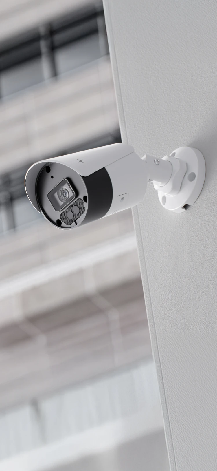 White outdoor security camera mounted on a textured wall with a blurred building in the background.