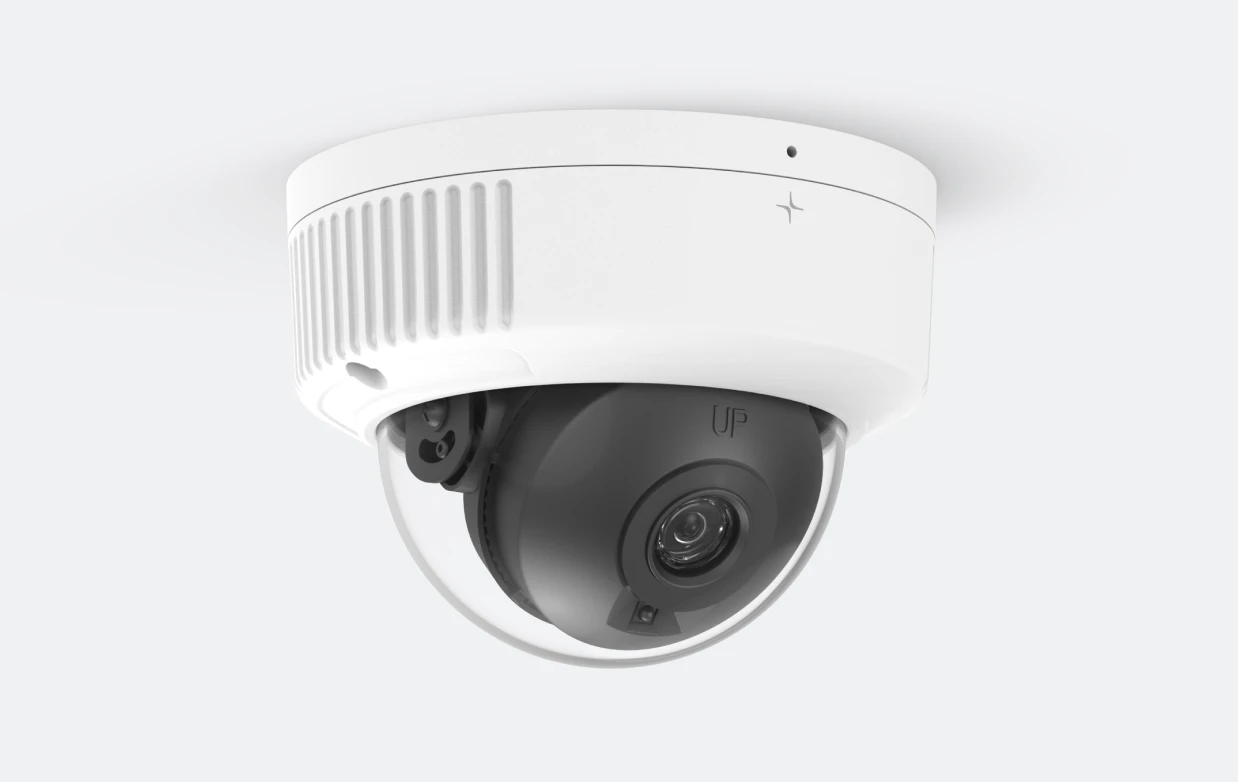 White dome security camera with a black inner lens housing mounted on a white ceiling.
