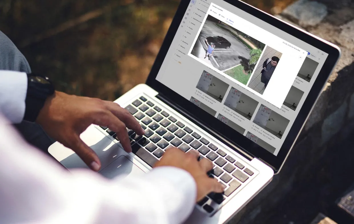 Person typing on laptop showing security camera footage and surveillance images on screen.