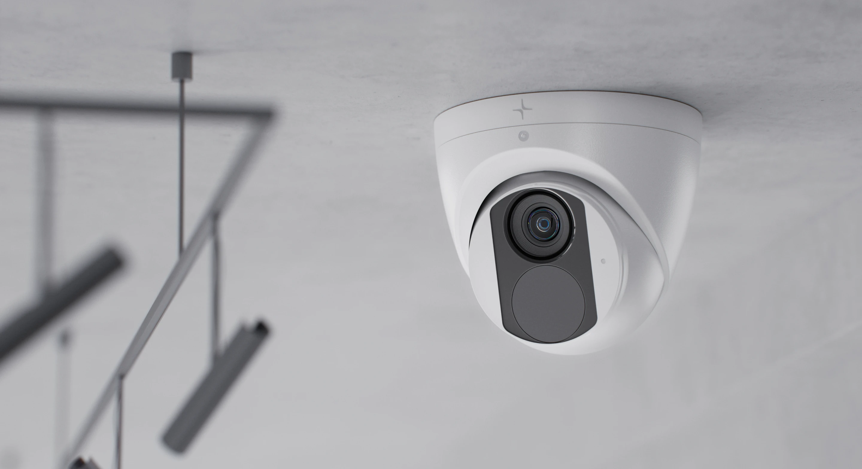 White security camera mounted on a gray ceiling near modern hanging lights.