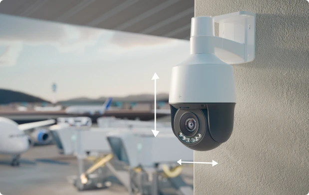 Security camera mounted on a wall overlooking an airport runway with airplanes in the background.