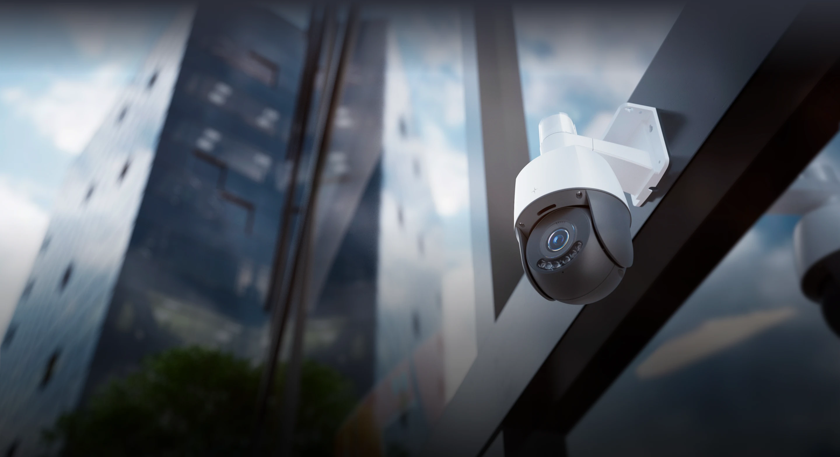 White security camera mounted on a building with reflective glass windows and blurred skyline background.