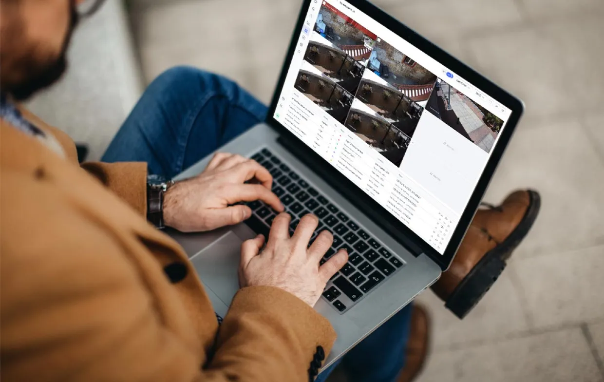 Person wearing brown coat and typing on laptop showing multiple security camera feeds on screen.