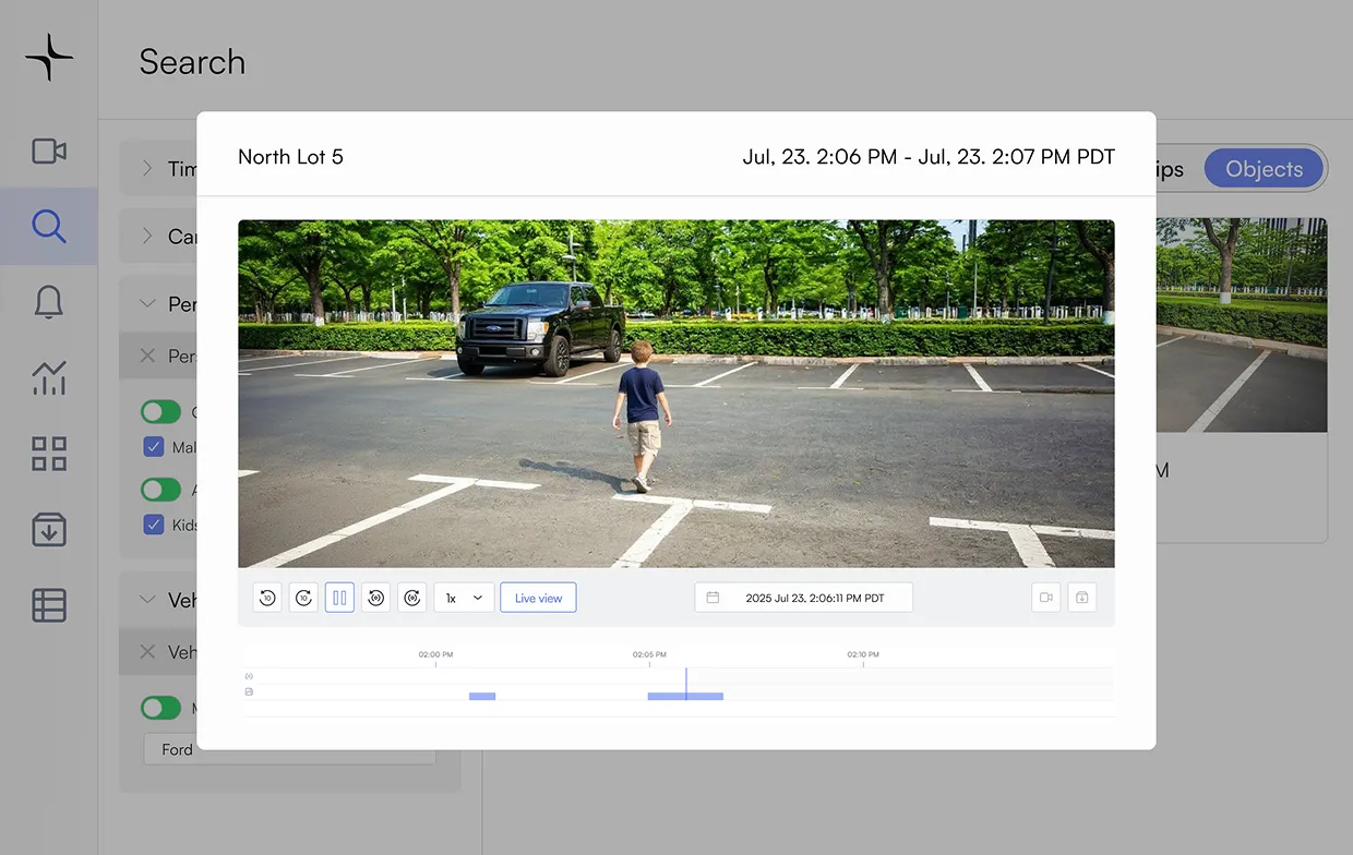 A boy walks in an empty parking lot with a black pickup truck parked near green trees in the background.