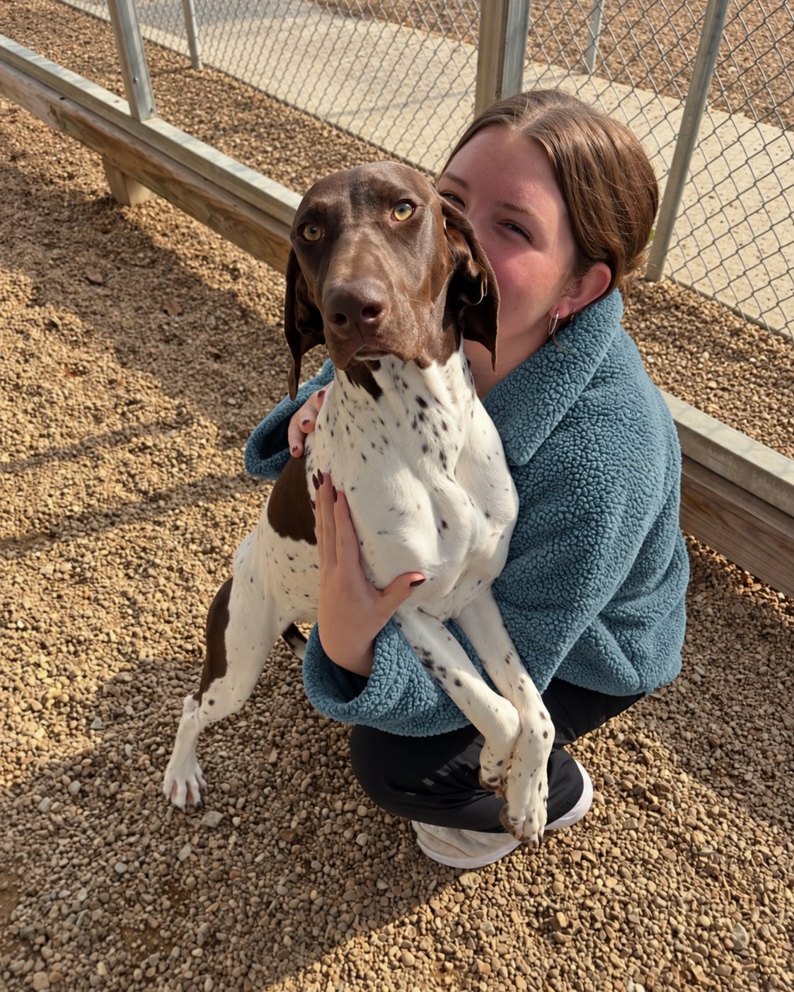 Pet Resorts of America team member hugging a German shorthaired pointer in the outdoor play yard