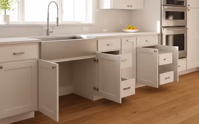 Modern kitchen with beige cabinets featuring open doors and drawers, a stainless steel sink, and built-in double oven.
