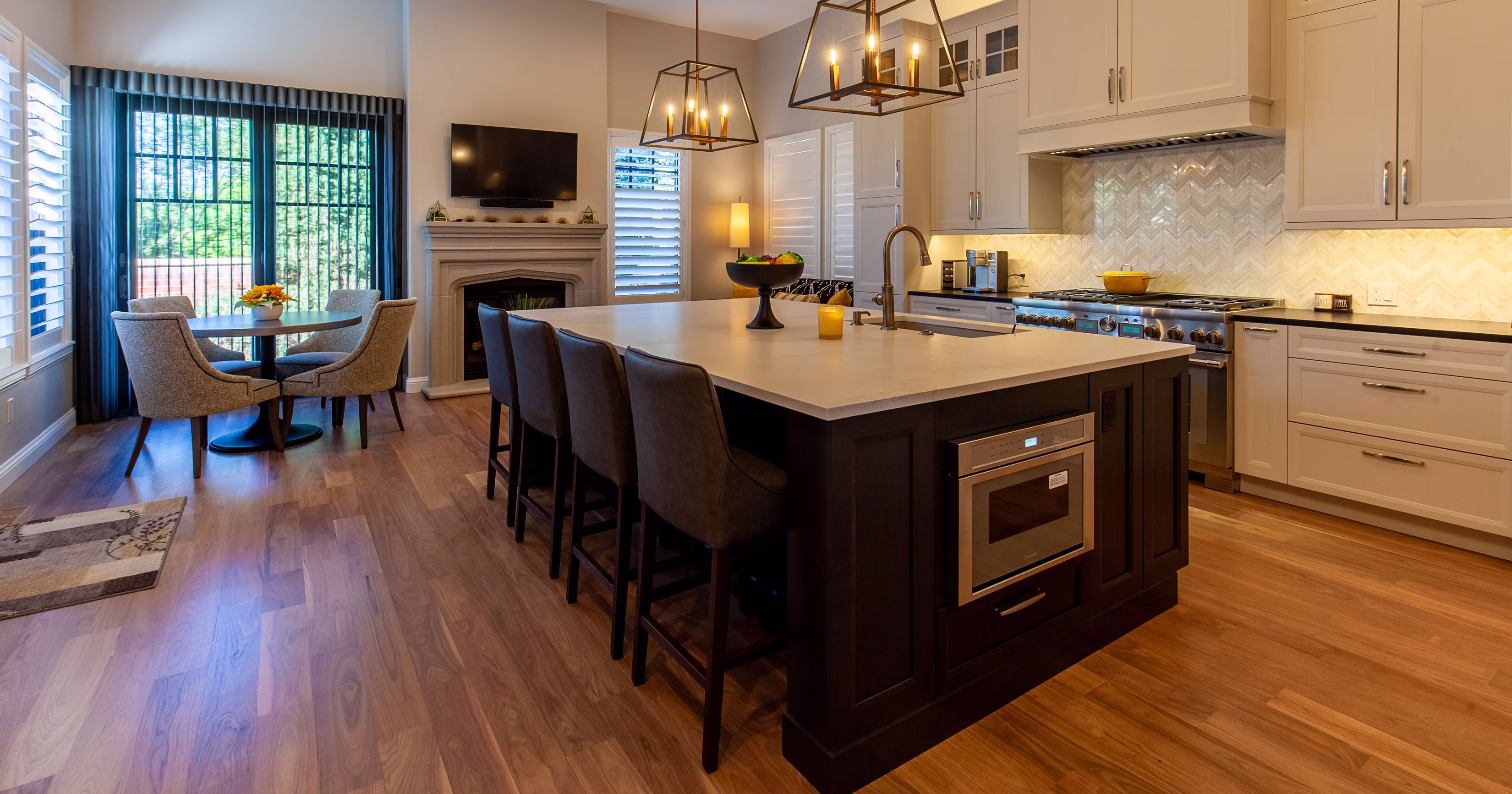 Modern kitchen with a large island, four chairs, dining table, fireplace, and stainless steel appliances.