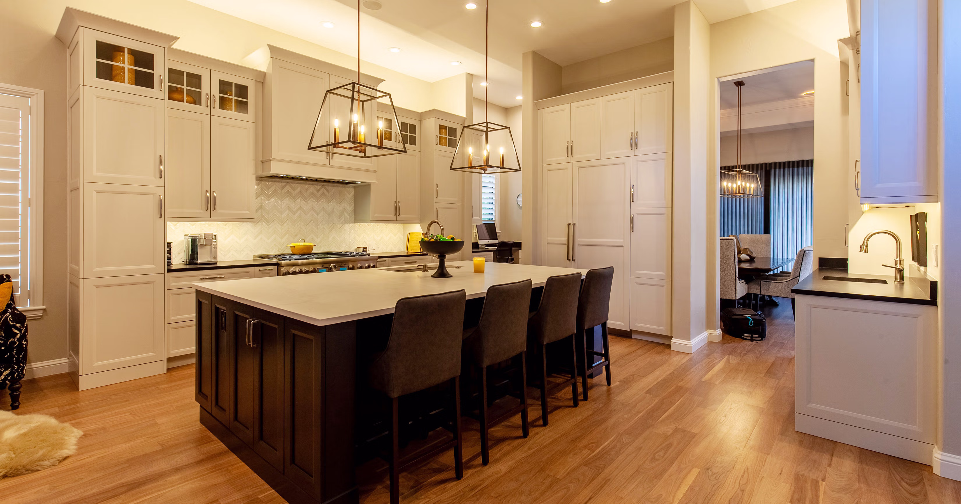 Modern kitchen with large center island, four chairs, pendant lights, white cabinets, and wooden floor.