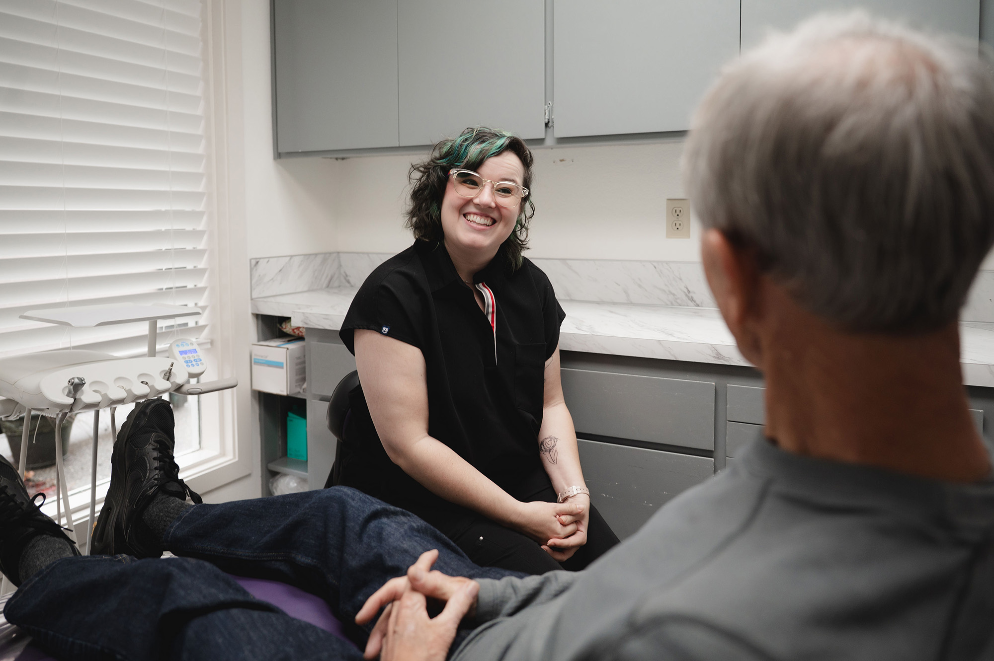 Smiling female dental professional consulting with an older male patient in a dental office.