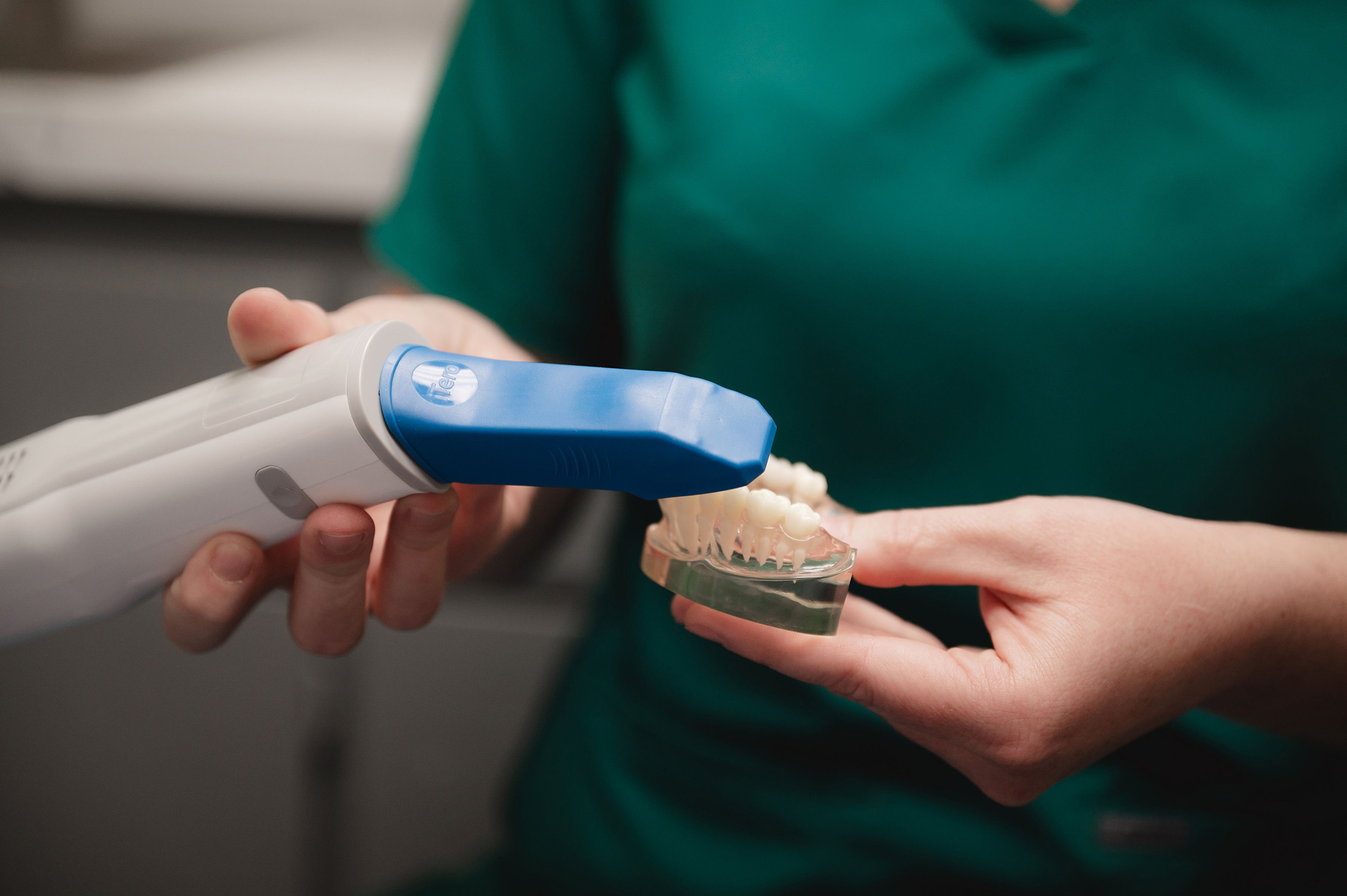 Person holding a dental scanner device close to a dental model of teeth.