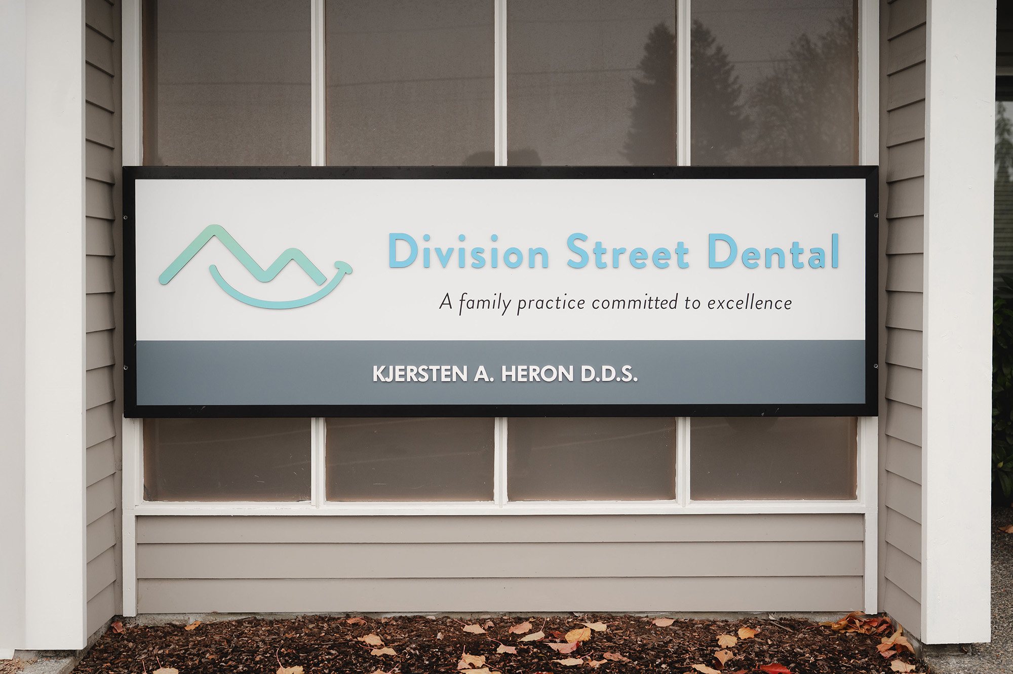 Division Street Dental sign with logo, slogan 'A family practice committed to excellence,' and name Kjersten A. Heron D.D.S.