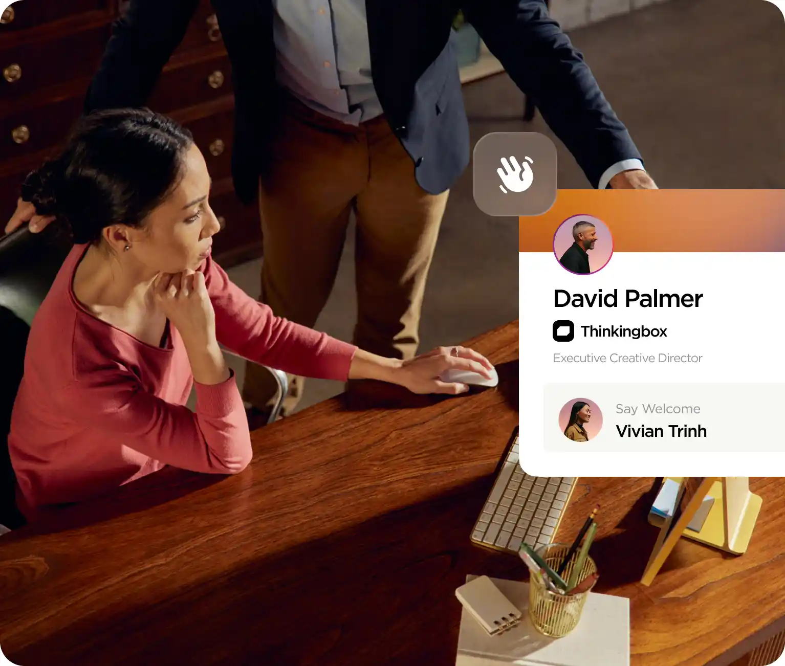 Woman seated at a wooden desk using a computer mouse while a man stands beside her, overlay showing a professional profile for David Palmer, Executive Creative Director at Thinkingbox.