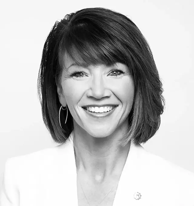 Black and white portrait of a smiling woman with short hair wearing hoop earrings and a white blazer.