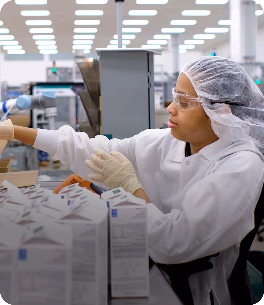 Factory worker wearing protective gear packing products in a production line.