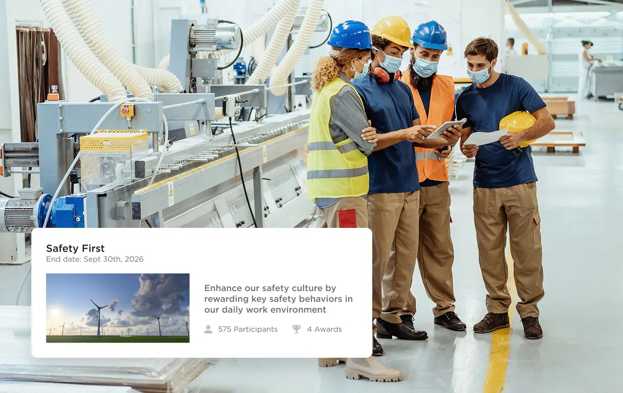 Four factory workers wearing safety helmets and masks reviewing a tablet in a manufacturing facility.
