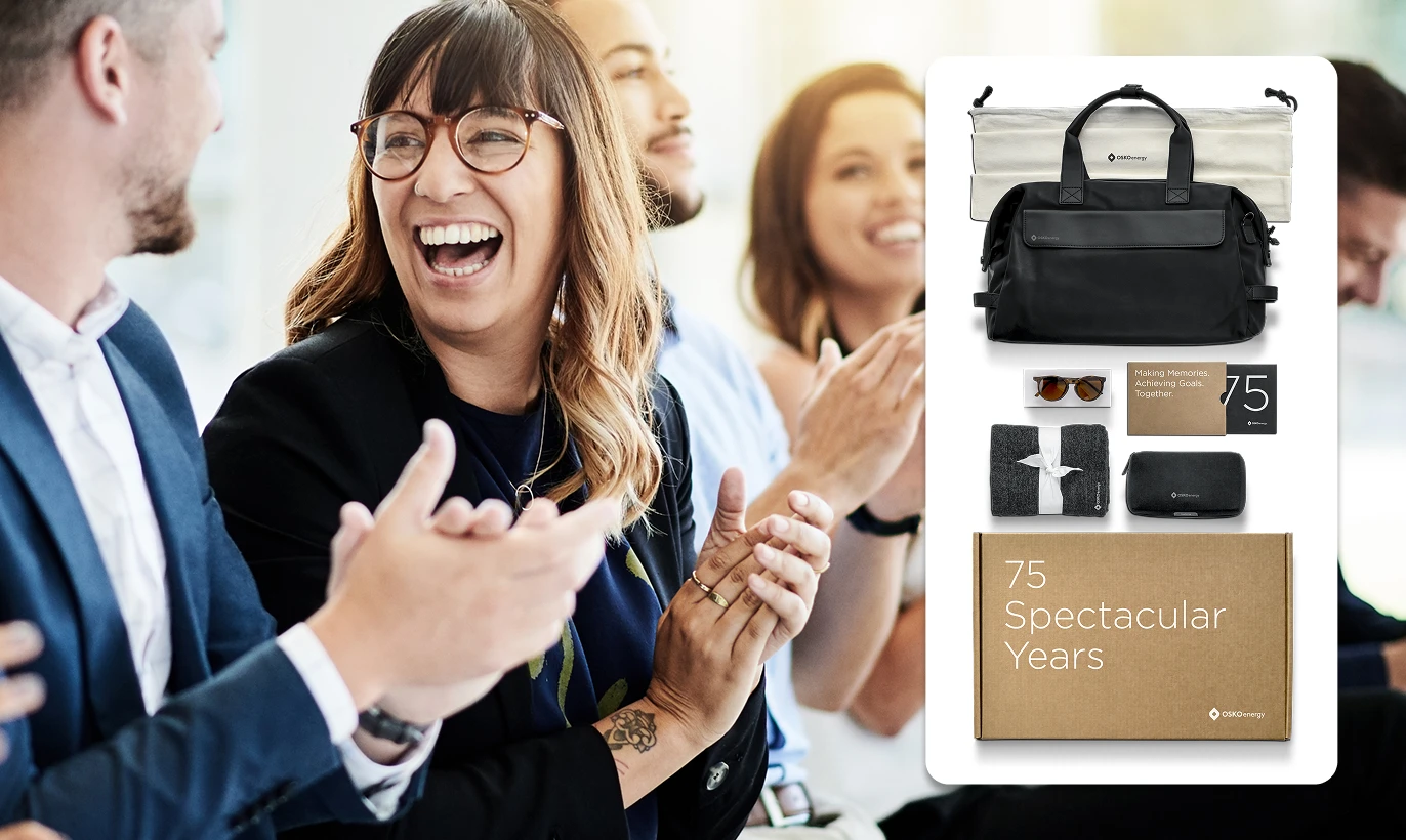 Group of diverse coworkers smiling and clapping with a superimposed image of a gift set including a black bag, blanket, sunglasses, and a box labeled '75 Spectacular Years'.