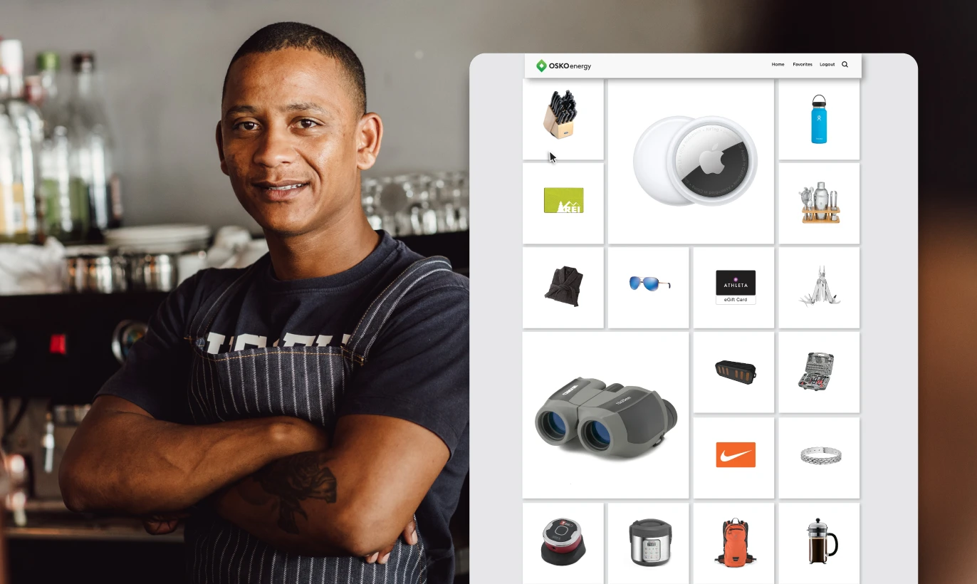 Man in apron standing with arms crossed in a kitchen or bar area next to a screen showing an online shopping grid with various products including binoculars, sunglasses, and kitchenware.