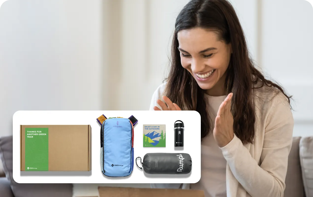 Smiling woman opening a box with green-themed outdoor gear including a souvenir box, blue pack, drink bottle, and sleeping bag.
