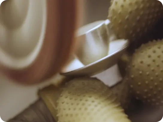 Close-up of a gloved hand polishing a curved metallic object with a spinning buffing wheel.