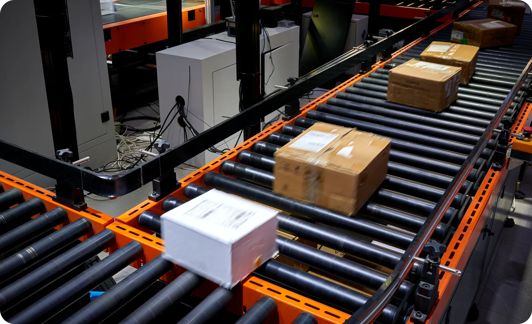 Several cardboard boxes moving on a roller conveyor belt in a warehouse or packaging facility.