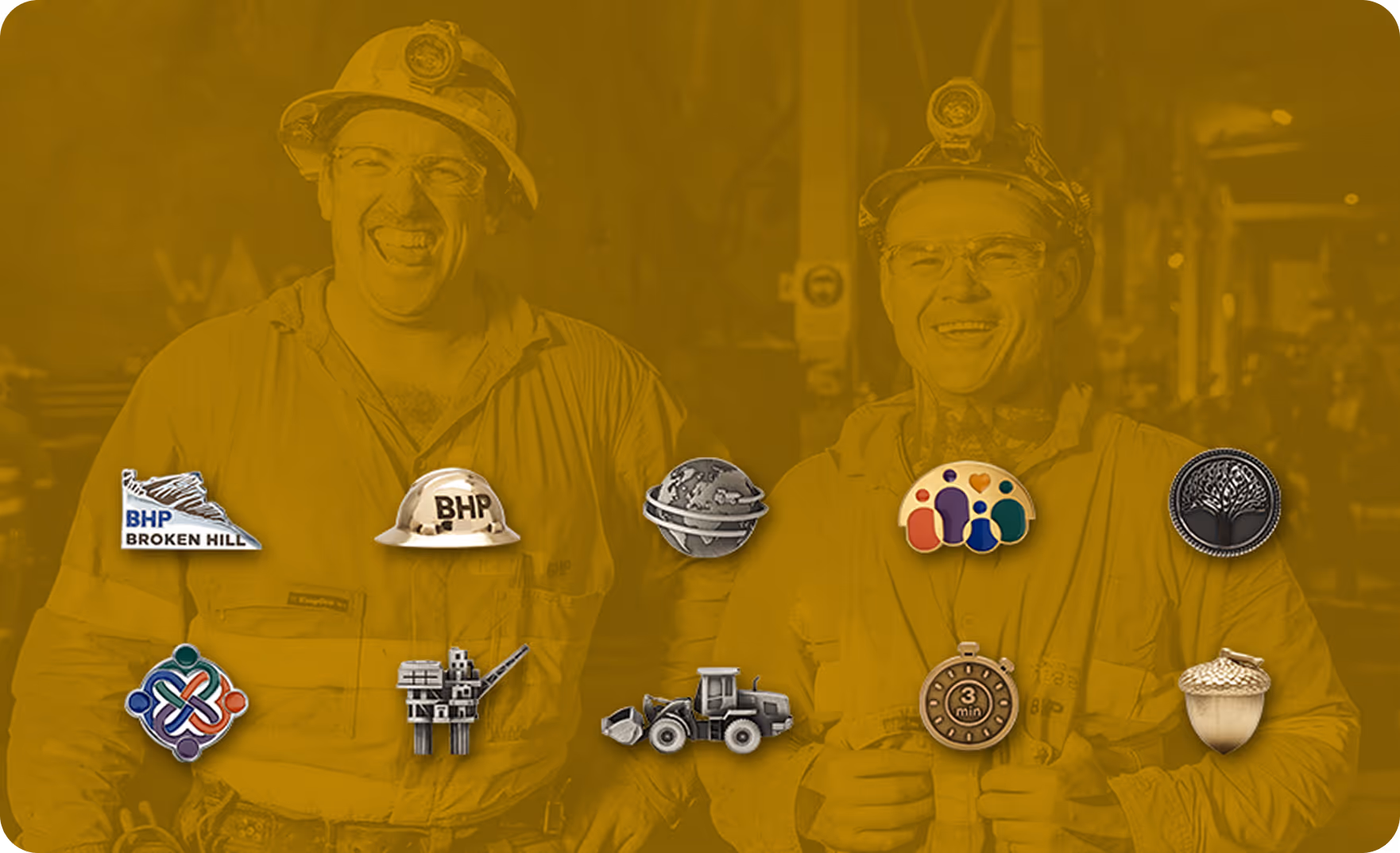 Two smiling miners in safety gear with nine metal pins in front, including a BHP Broken Hill pin, hard hat pin, globe pin, community pin, tree pin, colorful knot pin, offshore platform pin, bulldozer pin, timer pin, and acorn pin.